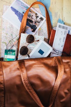 Flat lay of travel essentials including a leather bag, map, sunglasses, and tickets.