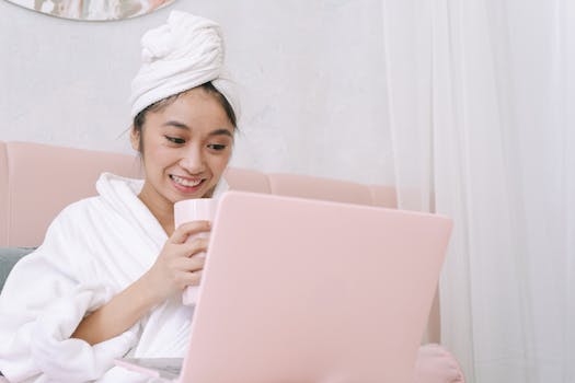 Young Asian woman enjoying leisure time with drink and laptop indoors.