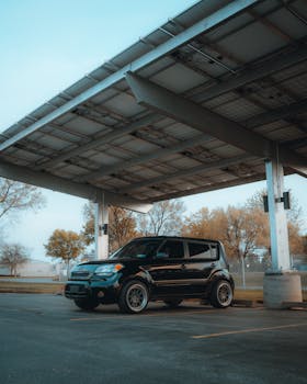 A black SUV parked under a large metal canopy in an outdoor parking lot with trees in the background.