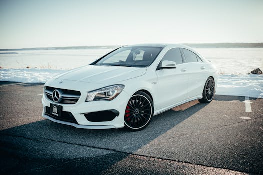 Sleek white Mercedes Benz sedan parked on a snowy road with a tranquil background.